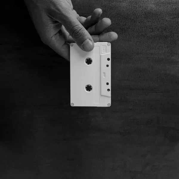 stock image A male hand gives a White magnetic audio tape on a wooden base. Audio cassette. Music. Black and white.