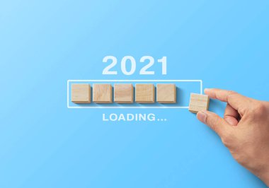 2021 yükleme, yeniden başlatma, yenileme veya zihniyet konsepti. Mavi arkaplandaki işlem çubuğuna ahşap bloklar yerleştiriliyor ve 2021 kelimesi yükleniyor.