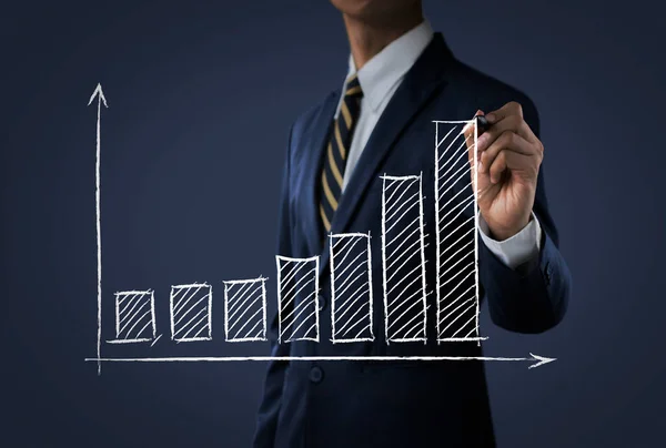 Business growth, progress or success concept. Businessman is drawing a growing bar graph on dark tone background.