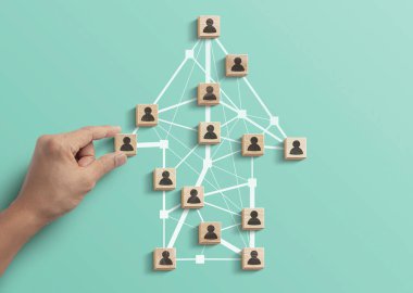 İnsan kaynakları yönetimi, takım çalışması yönetimi ya da başarı konseptine iş stratejisi. El, turkuaz arka planda çokgen ok şeklindeki insan simgesiyle ahşap blokları düzenliyor.
