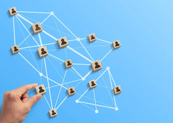 Human resources management, teamwork management or business strategy to success concept. Hand is arranging wooden blocks with human icon in polygon rocket shape network on blue background.