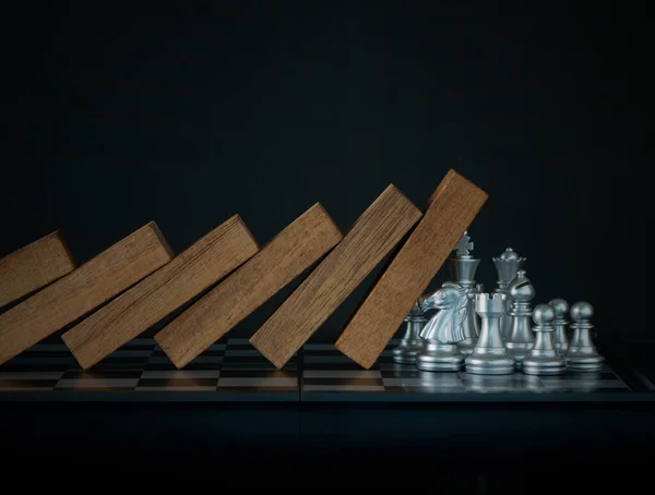 Crisis management, risk management, crisis solving or problem solving concept. Chess stopping wooden dominoes from collapsing on chessboard in black scene.