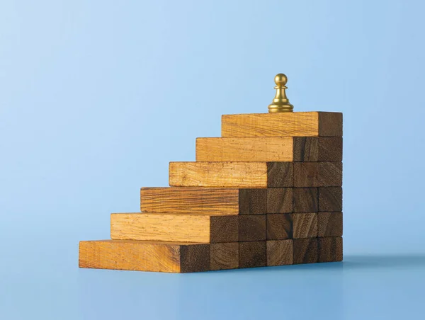 Business growth, business success or career path success concept. A pawn chess is on the top of wooden stacked staircase in blue scene background.
