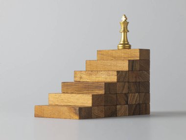 İş büyümesi, iş başarısı ya da kariyer yolu başarı kavramı. Beyaz sahne arka planında tahta merdivenlerin üzerinde bir kral satrancı var..