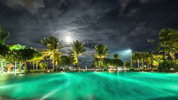 Piscina noturna iluminada contra o pano de fundo das palmeiras e do mar. 4K Timelapse - Bali, Indonésia, junho de 2016 . — Vídeo de Stock