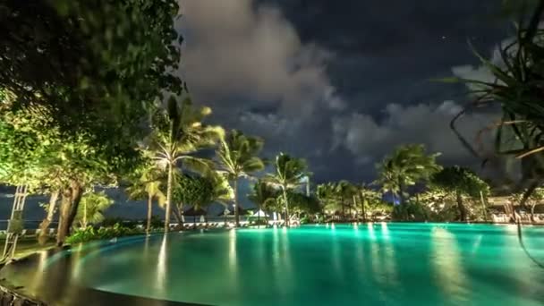 Des nuages flottent au-dessus de la piscine nocturne éclairée sur fond de palmiers et de mer. 4K Timelapse - Bali, Indonésie, juin 2016 . — Video