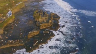 Turist kalabalığı, Endonezya 'nın en sevilen dramatik günbatımı sahnelerinden biri olan Hindu tapınağı Pura Tanah' a doğru ilerliyor. Hava görüntüsü 4K