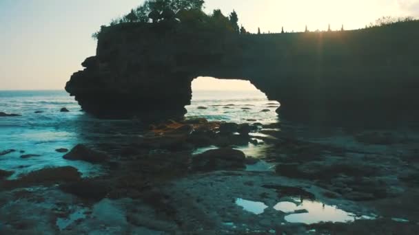 Pura Batu Bolong sul bordo di una scogliera sulla costa con buco nella roccia all'ora del tramonto a Bali, Indonesia. Vista aerea 4K — Video Stock