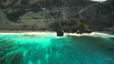 Endonezya 'daki Nusa Penida, Bali' deki tropik adanın kayalık arka planındaki cennet kumsalındaki deniz dalgalarının güzel manzarası. Hava görüntüsü 4K