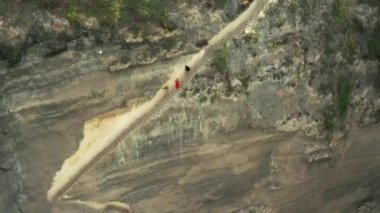 Turistler, Endonezya 'nın Bali adasındaki Nusa Penida Adası' ndaki Diamond Beach 'teki bir kayada kesilen dik bir merdivenden tırmanıp iniyorlar. Hava görüntüsü 4K