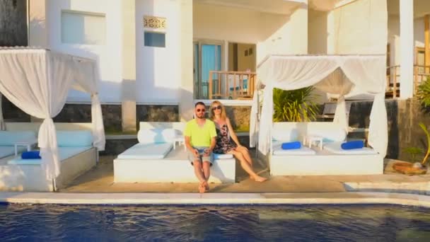 Šťastnou dovolenou v krásném hotelu na pláži při západu slunce, muž a žena sedí v blízkosti bazénu a relaxaci s panoramatickým výhledem na moře. Letecký pohled 4K — Stock video