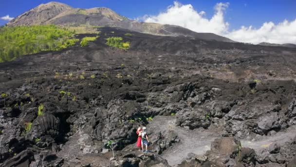Joven pareja de excursionistas en el campo de lava negro en el volcán Batur en Kintamani, Bali, Indonesia. Vista aérea 4K — Vídeos de Stock