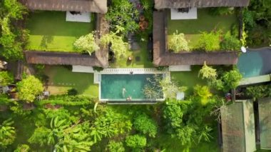 Mutlu aile Ubud, Bali, Endonezya 'da tropikal bir otelde lüks bir sonsuzluk havuzunda yüzer ve dinlenir. Anhera Süit Spa, Ubud, Bali, Endonezya - 15 Temmuz 2019. Hava görüntüsü 4K.