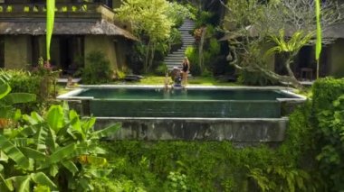 Ubud, Bali, Endonezya 'daki tropik bir cennette sonsuz havuzun kenarında oturan mutlu bir aile. Anhera Süit Spa, Ubud, Bali, Endonezya - 15 Temmuz 2019.