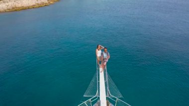 İHA uçup giderken denizdeki bir geminin pruvasında oturan çift manzarayı gözler önüne seriyor. Kekova, Kas, Türkiye. Hava görüntüsü 4K.