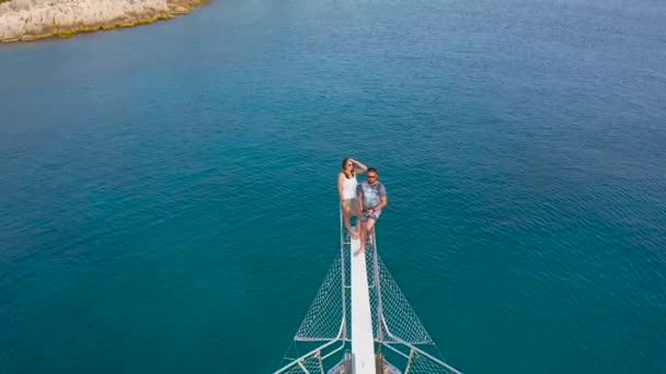 Couple assis sur la proue d'un navire dans la mer tandis que le drone s'envole révélant un paysage panoramique. Kekova, Kas, Turquie. Vue aérienne 4K. — Video