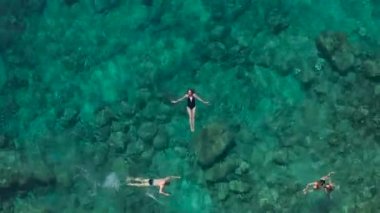Siyah bikinili genç bayanın havadan görünüşü turkuaz denizde yüzüyor. Sıska bir kadının denizin üzerinde yüzüşünün en üst görüntüsü.