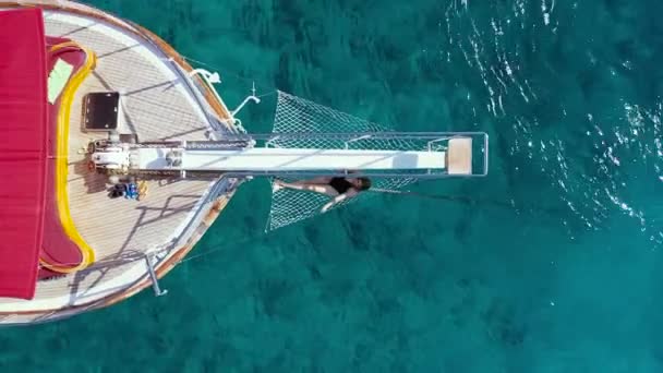 Menina de biquíni encontra-se rede na proa de um iate contra o pano de fundo do mar. Vista aérea 4K. — Vídeo de Stock