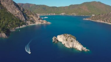 Okyanustaki ve kayalıklardaki ada ve kayalar, deniz kıyısı mavi Marmaris, Icmeler Türkiye 'deki dağların arka planında dinleniyor. Hava görüntüsü 4K.