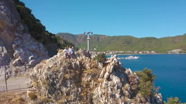 Fiatal pár ül egy sziklán az Égei-tenger partján hátterében hegyek és az öböl Icmeler, Marmaris, Mugla tartomány, Törökország. Légi felvétel 4K. — Stock videók
