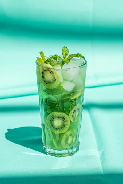 Kiwi-Limettengetränk mit Minze und Eis im Glas in Nahaufnahme auf türkisfarbenem Hintergrund. — Stockfoto