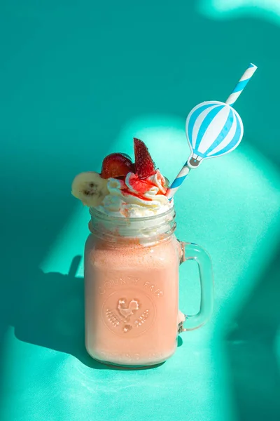 Strawberry milkshake with whipped cream on colorful turquoise background with abstract shadows.