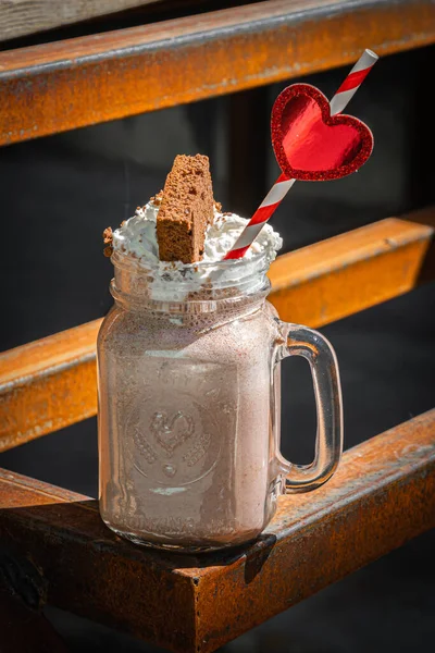 Milkshake chocolate with whipped cream and cake on rusty construction background.