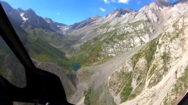 Helikopter kokpitinden kayalık dağlar ve göl manzarası.