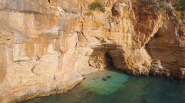 Bir çift gezgin Demre 'den Antalya, Türkiye' ye giden yolda dağda mağarası olan gizli bir koyda yüzüyor. Hava görüntüsü 4K.