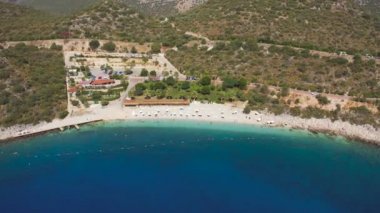 Gök mavisi denizde yüzen ve Türkiye 'nin Kas, Antalya kentindeki dağların arka planında güneşlenen turistler. Hava görüntüsü 4K.