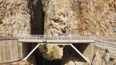 Genç çift, Türkiye 'deki Kaputas plajı ve kayaların arasındaki köprüde duruyor. Hava görüntüsü 4K.