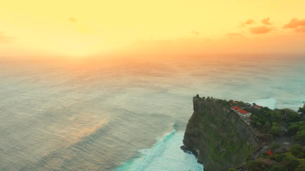 Αεροφωτογραφία σε μεγάλα κύματα του ωκεανού και βράχους κατά τη διάρκεια του ηλιοβασιλέματος στο Ναό Uluwatu, στο νησί Μπαλί, Ινδονησία — Αρχείο Βίντεο