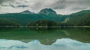 Dağlar, bulutlu bir günde Durmitor Ulusal UNESCO parkındaki Kara Göl 'ün suyuna yansıyor. Zaman Dilimi 4K.