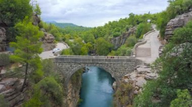 Koprulu Kanyonu 'ndaki eski köprüde turistler. Manavgat, Antalya, Türkiye - 20 Kasım 2020. Hava görüntüsü 4K.