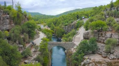 Koprulu Kanyonu 'ndaki eski köprüde turistler. Manavgat, Antalya, Türkiye - 20 Kasım 2020. Hava görüntüsü 4K.