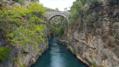 İnsansız hava aracı, Türkiye 'nin Antalya kentindeki Koprulu kanyonundaki fırtınalı bir nehrin üzerindeki eski bir köprünün altından uçuyor. Hava görüntüsü 4K