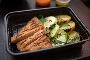 Izgarada kızarmış et ve siyah bir masada plastik ambalajda kabak.