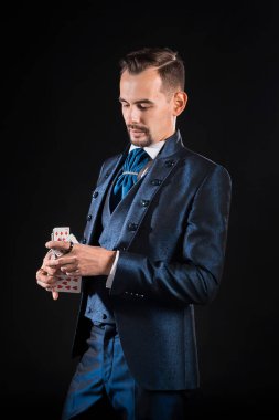 Mavi ceketli bir sihirbaz, elindeki iskambil kağıtlarına dikkatlice bakar.