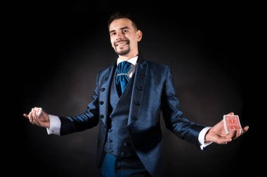 Siyah arka planda mavi ceketli bir sihirbaz elinde kartları tutuyor.