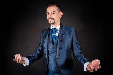 Siyah arka planda mavi ceketli bir sihirbaz elinde kartları tutuyor.