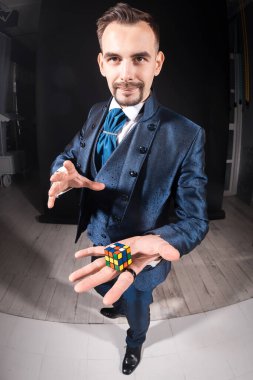 Mavi ceketli yakışıklı erkek sihirbaz elinde Rubik küpü tutuyor.