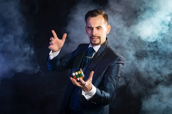 A magician in a blue tailcoat levitates with a rubik\'s cube