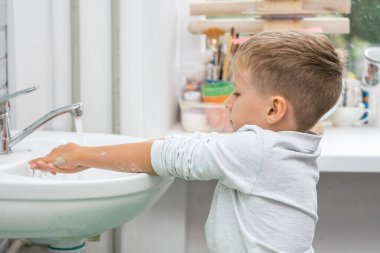 Beyaz gömlekli bir çocuk ellerini çamurdan yıkıyor.