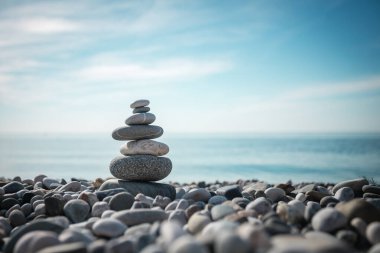 Açık mavi gökyüzünün arka planına karşı deniz kıyısında gri taşlardan oluşan bir sütun..