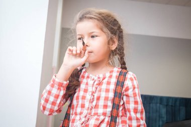 Ekose gömlekli bir kız burnuna kelebek dikmeye çalışıyor..