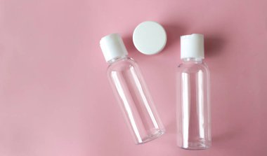 Pembe arka planı beyaz kapaklı plastik şeffaf kozmetik şişeler.