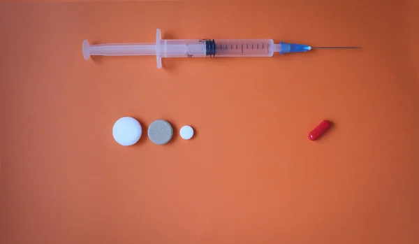 Medicinsk spruta med nål och tabletter på orange bakgrund. Flerfärgade tabletter på en färgad bakgrund. — Stockfoto