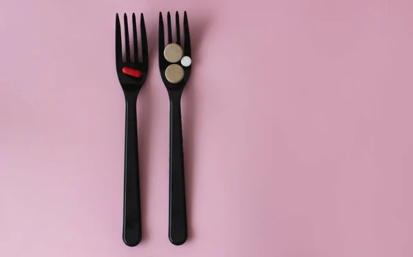 İki siyah plastik çatal ve pembe arka planda renkli tabletler..