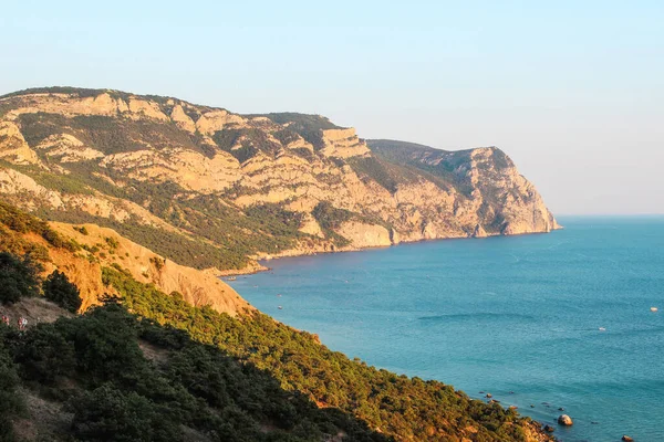 Büyük bir dağın, denizin ve ağaçların arkasında gün batımı. Bear Dağı. Kırım.