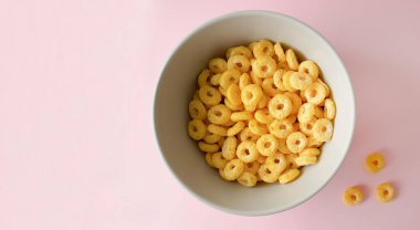 Pembe arka planda bir kase kahvaltı gevreği. Sağlıklı gevrek halkaları. Mesaj için yer var. Üst Manzara. Düz yatıyordu.